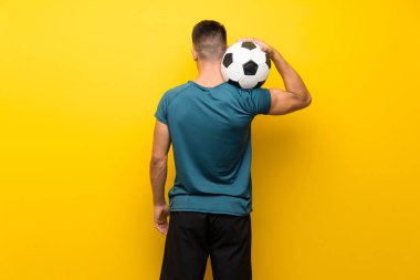 İzole edilmiş sarı arka planda yakışıklı genç futbolcu.