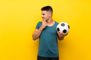 Yakışıklı genç futbolcu, izole edilmiş sarı arka planda bir fikir ve bakış açısı düşünüyor.