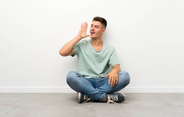 Genç yakışıklı adam yerde oturuyor ve ağzı açık bağırıyor.