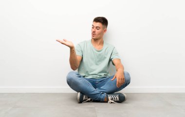 Genç yakışıklı bir adam yerde oturuyor. Elinde hayali bir fotokopi makinesi var.