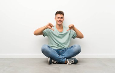 Genç yakışıklı adam yerde oturmuş gururlu ve kendinden memnun.