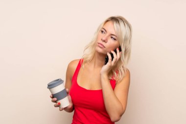 Arka planda izole edilmiş genç sarışın kadın elinde kahve ve bir cep telefonu tutuyor.