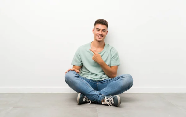 Genç Yakışıklı Adam Yerde Oturuyor Parmağını Yana Doğru Gösteriyor — Stok fotoğraf