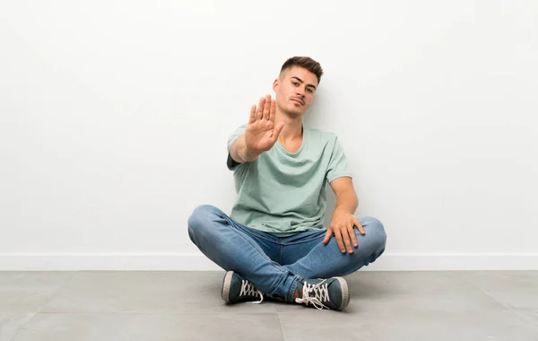 Mladý Pohledný Muž Sedí Podlaze Dělat Stop Gesto Její Rukou — Stock fotografie