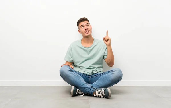 Junger Gutaussehender Mann Sitzt Auf Dem Boden Und Zeigt Mit — Stockfoto