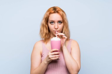 Izole mavi arka plan üzerinde çilek milkshake ile genç kadın