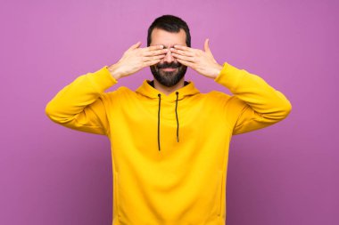 Sarı kazaklı yakışıklı adam gözlerini elleriyle kapatıyor.