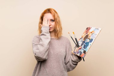 İzole edilmiş arka planda genç bir sanatçı kadın. Göz kapağını elleriyle kapatıyor.