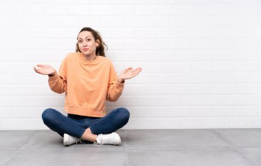 Yerde kıvırcık saçlı genç bir kadın oturuyor. Kafası karışık bir yüz ifadesi var.