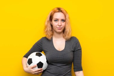Bir futbol topu tutan izole sarı arka plan üzerinde genç kadın