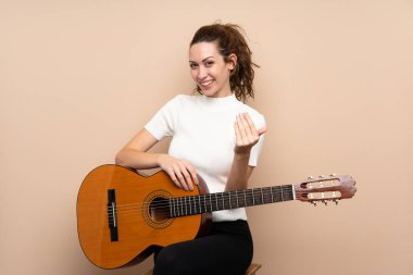 Arka planda gitarı olan genç bir kadın benimle gelmesi için davet ediyor. Gelmene sevindim.