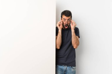 Sakallı, genç ve yakışıklı bir adam elinde kocaman boş bir pankart, gözlüklü ve şaşırmış.