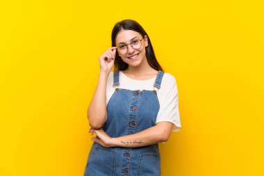 Sarı arka planda, gözlüklü ve mutlu bir kadın.