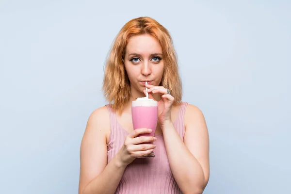 Izole mavi arka plan üzerinde çilek milkshake ile genç kadın — Stok fotoğraf