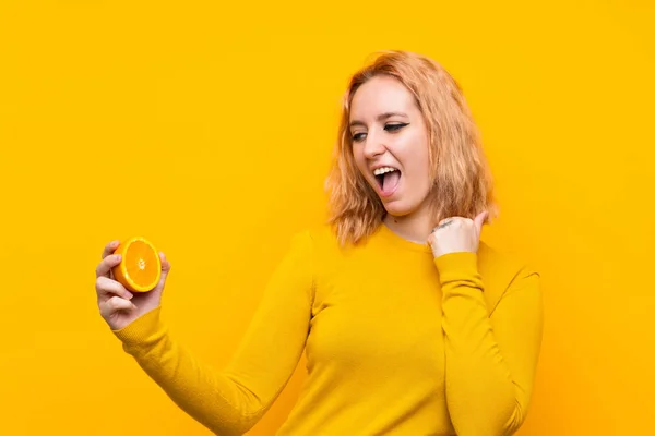 Sarı Arka Planda Portakal Tutan Genç Bir Kadın Zaferi Kutluyor — Stok fotoğraf