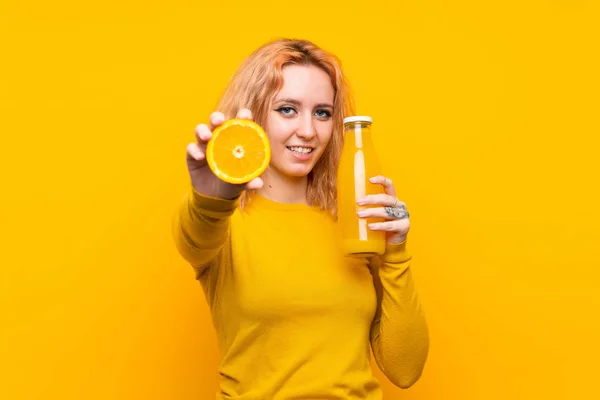 Junge Frau hält eine Orange über einem isolierten gelben Hintergrund — Stockfoto