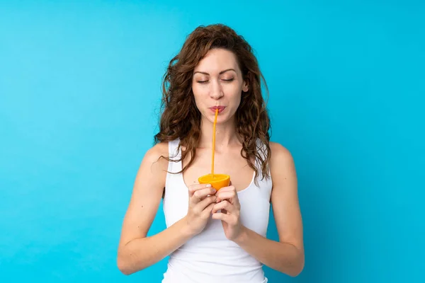 Kıvırcık saçlı genç bir kadın portakalı mavi arka planda tutuyor. — Stok fotoğraf