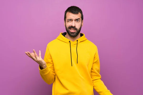 Handsome man with yellow sweatshirt making doubts gesture