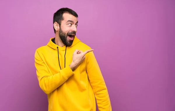 Handsome man with yellow sweatshirt surprised and pointing side