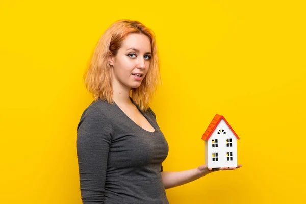 Jonge Vrouw Geïsoleerde Gele Achtergrond Houden Een Klein Huis — Stockfoto