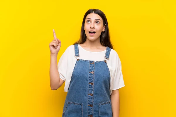 Young Woman Dungarees Isolated Yellow Background Pointing Surprised — ストック写真