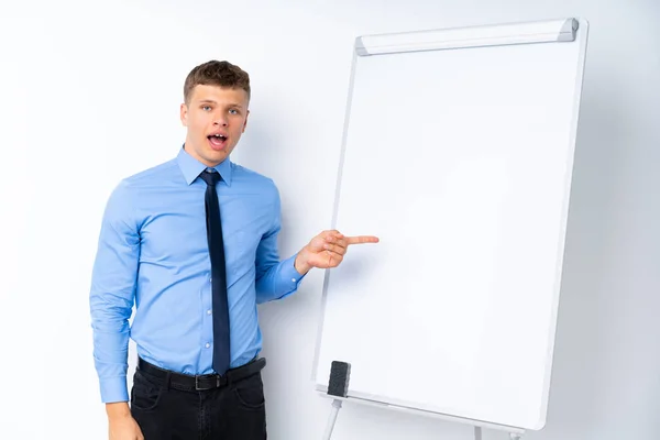 Young businessman giving a presentation on white board surprised and pointing finger to the side