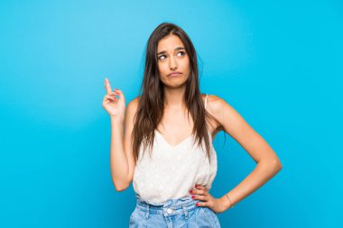 İzole edilmiş mavi arka planı olan genç bir kadın parmaklarını çapraz yapıp en iyisini diliyor.