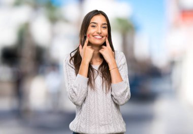 Açık havada mutlu ve hoş bir ifadeyle gülümseyen esmer Latin bir kadın.