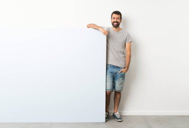 Sakallı genç yakışıklı adam elinde kocaman mavi bir pankart tutarak gülüyor.