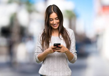 Genç İspanyol esmer kadın dışarıda cep telefonuyla mesaj yolluyor.