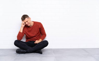 Genç yakışıklı adam yerde oturmuş gülüyor.