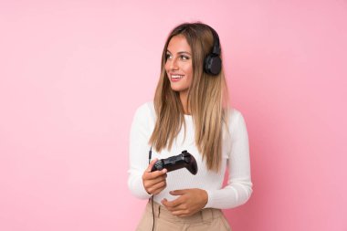 İzole edilmiş pembe arka planda video oyunlarında oynayan genç sarışın kadın.
