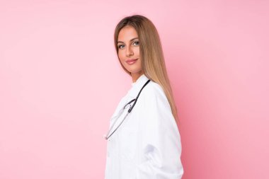 Doktor önlüğüyle izole edilmiş pembe arka planı olan genç sarışın kadın.