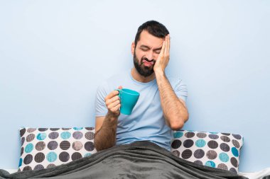 Bir fincan kahve tutan sakallı adam yatakta