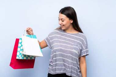 Alışveriş torbaları bir sürü tutan izole mavi arka plan üzerinde genç esmer kadın