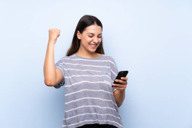 Cep telefonu kullanarak izole mavi arka plan üzerinde genç esmer kadın