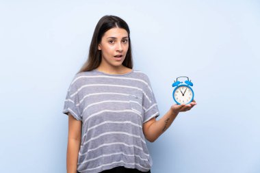 Vintage çalar saat tutan izole mavi arka plan üzerinde genç esmer kadın