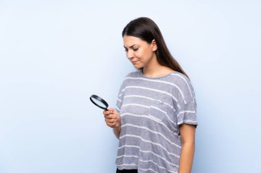 Bir büyüteç tutan izole mavi arka plan üzerinde genç esmer kadın