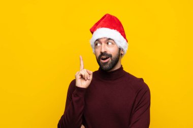 İzole edilmiş sarı arka plan üzerinde noel şapkası olan bir adam bir fikri işaret ederek...