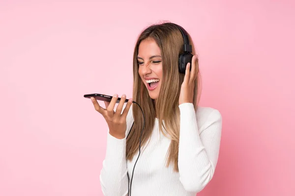 Joven Rubia Sobre Fondo Rosa Aislado Usando Móvil Con Auriculares —  Fotos de Stock