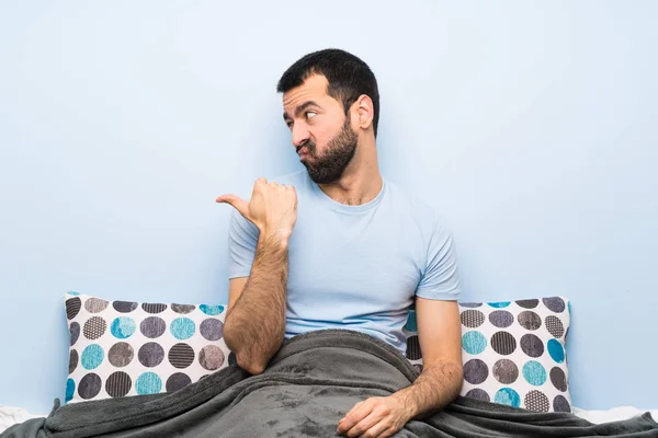 Man in bed unhappy and pointing to the side