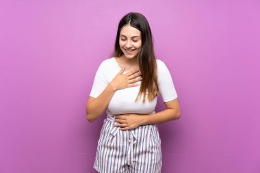 İzole edilmiş mor arka planı olan genç bir kadın çok gülümsüyor.