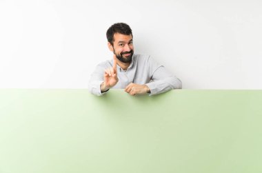 Sakallı genç yakışıklı adam yeşil boş bir pankart tutuyor ve parmağını kaldırıyor.