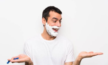 Adamın sakalını soyutlanmış beyaz arka planda tıraş etmesi. Kopyalama alanını iki eliyle tutuyor.