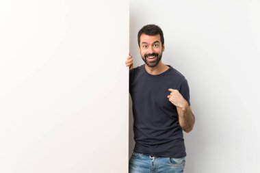 Sakallı genç yakışıklı bir adam elinde kocaman boş bir levha tutuyor.