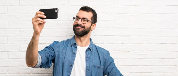 Przystojny Mężczyzna Brodą Nad Białą Ceglaną Ścianą Robi Selfie — Zdjęcie stockowe