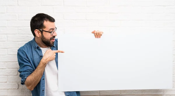 Bonito homem com barba sobre parede de tijolo branco segurando um cartaz vazio — Fotografia de Stock