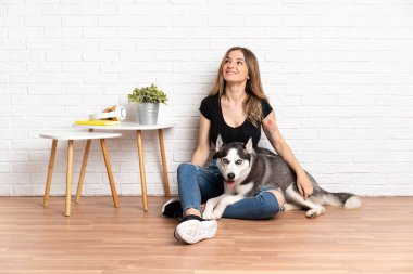 Genç ve güzel bir kadın, köpeğiyle yerde oturmuş gülümserken yukarı bakıyor.
