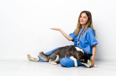 Sibiryalı Husky köpeği olan veteriner doktor yere oturmuş, davet etmek için ellerini yana uzatıyor.