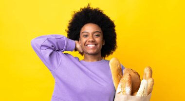 Genç Afrikalı Amerikalı bir kadın sarı arka planda izole edilmiş bir ekmek alıyor.